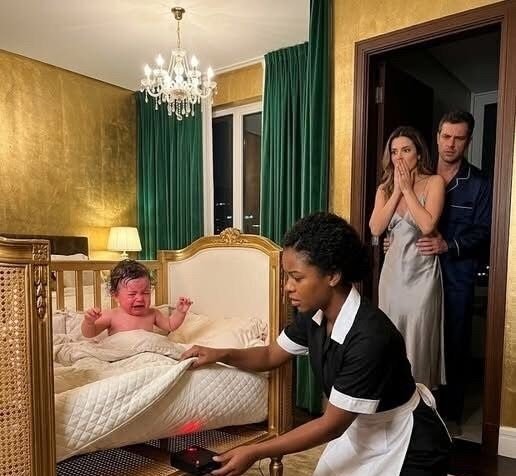 A nanny kneels beside a luxurious crib, her hand revealing a hidden panel with a blinking black device, while the wealthy parents stand in stunned horror in the background.