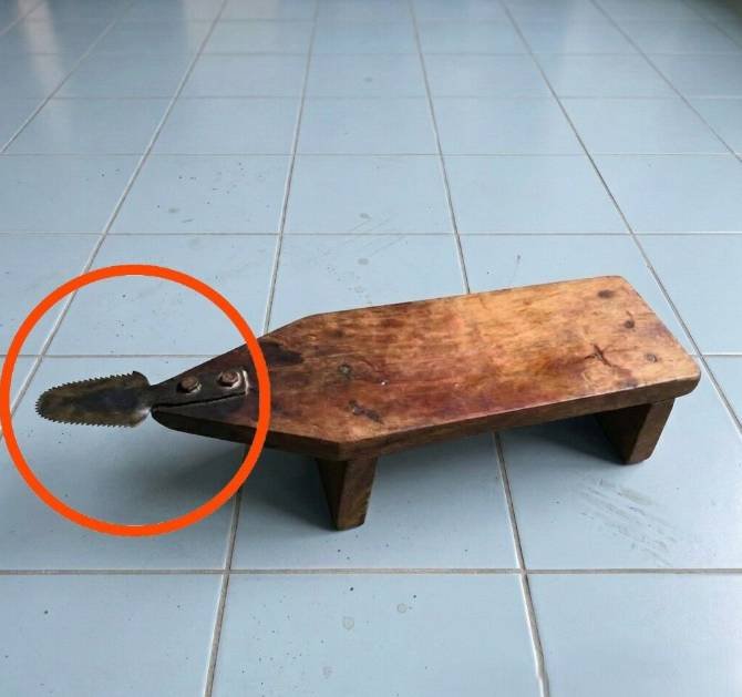 A traditional wooden coconut scraper stool with a serrated metal blade, used for grating coconut in tropical cooking practices.