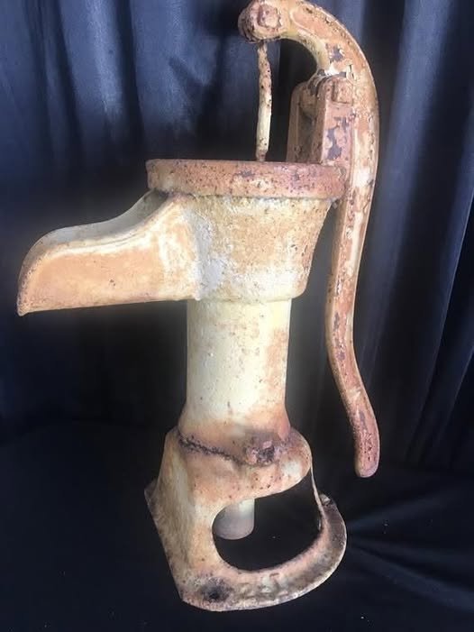 Old rusty cast iron hand water pump in a rural backyard, used historically to draw water from underground wells.