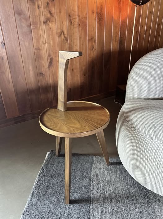 A Cicognino table in a cozy living room, its elegant handle and slender legs highlighted by warm lamplight, with a book and glass of wine resting on its surface.